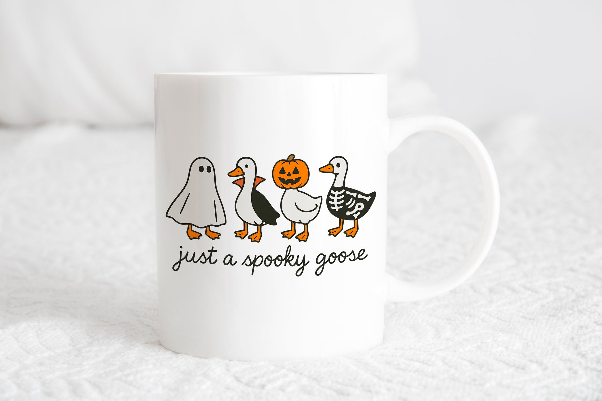 A white mug with a Halloween-themed design featuring four cartoon ducks, including a ghost and a jack-o-lantern, along with the text "just a spooky goose".