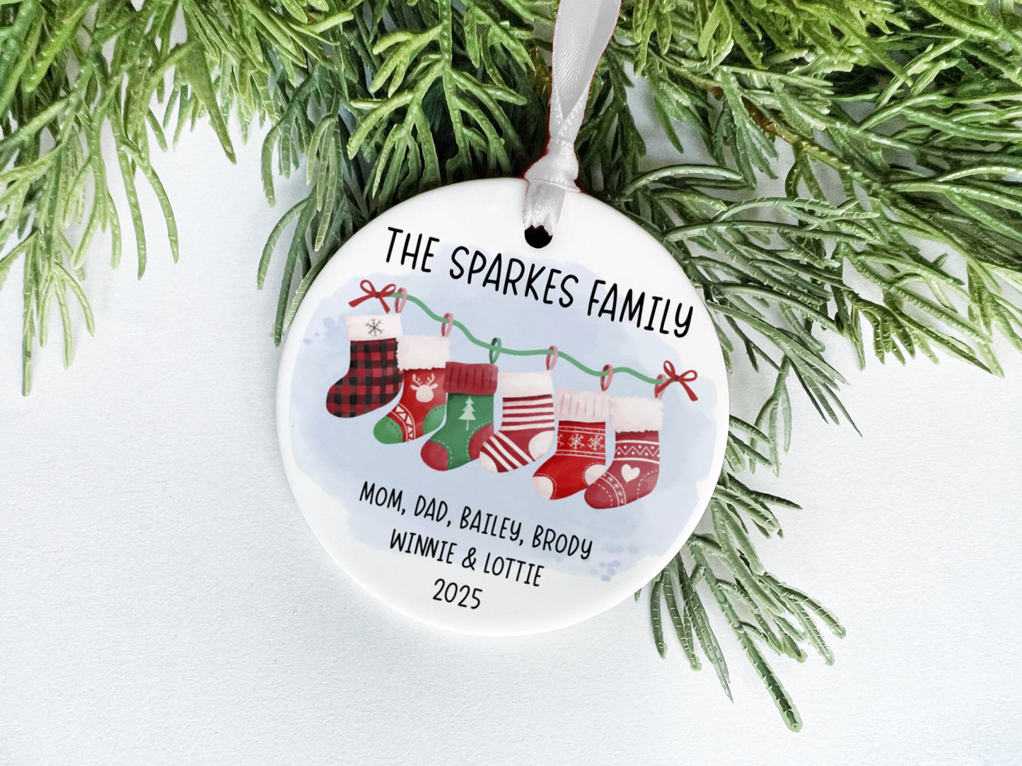 A white ceramic ornament with a Christmas tree branch and greenery, featuring a family tree design with the text "THE SPARKLES FAMILY" and the names "MOM, DAD, BAiley, BRODY, WINNIE & LOTTIE" along with the year "2025".