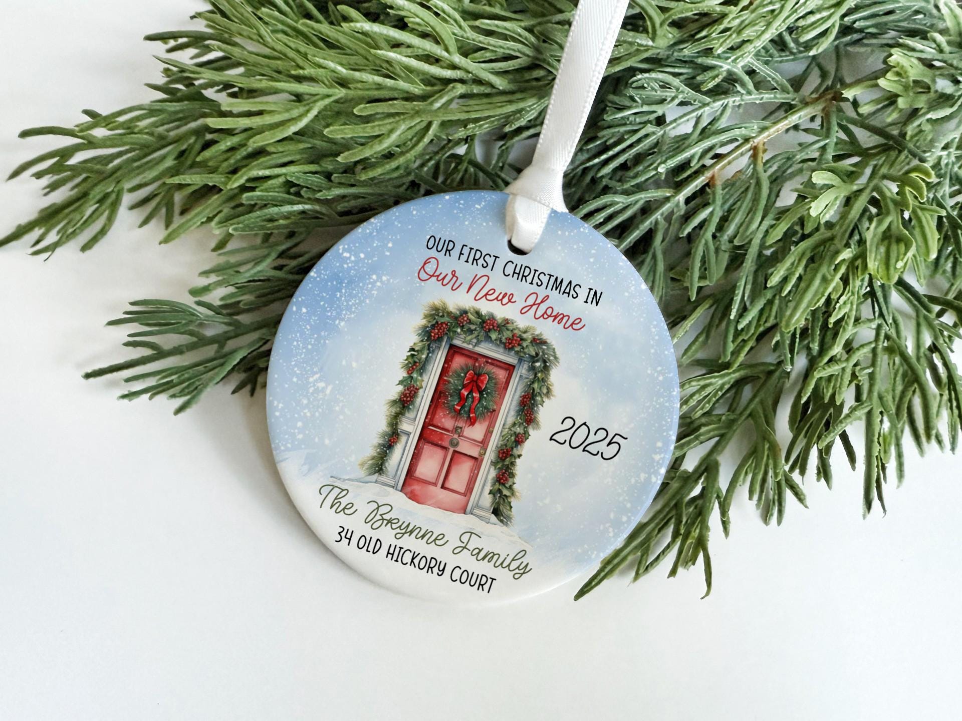 A Christmas ornament with a red door and wreath, hanging on a branch of a pine tree.
