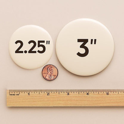 a ruler and two circular buttons, one labeled "2.25" and the other labeled "3.25", placed next to a penny for scale.