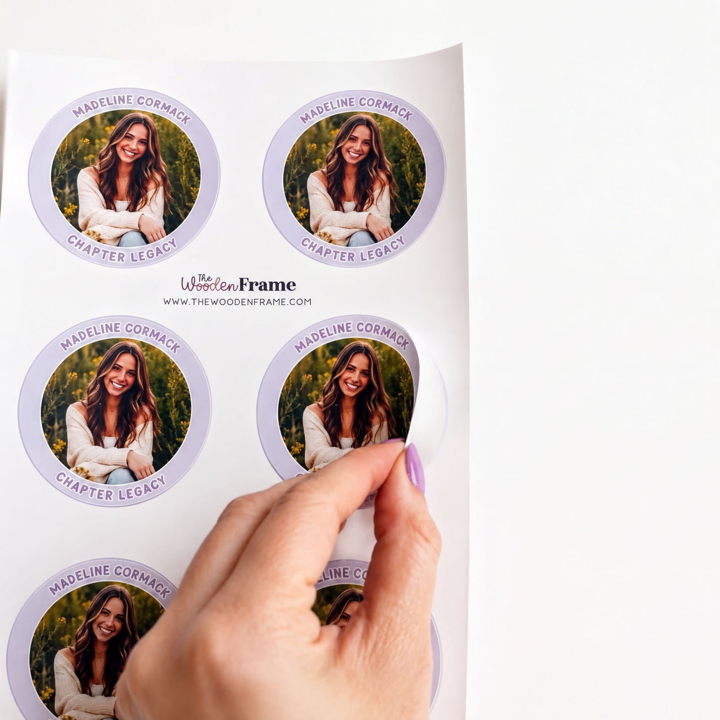 A hand is holding a sticker with a photo of a smiling woman, and the sticker is being peeled off a white surface.
