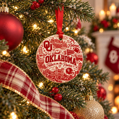 Oklahoma Sooners crimson and cream ceramic Christmas ornament hanging on a decorated tree with red ornaments, holiday lights, and festive greenery.