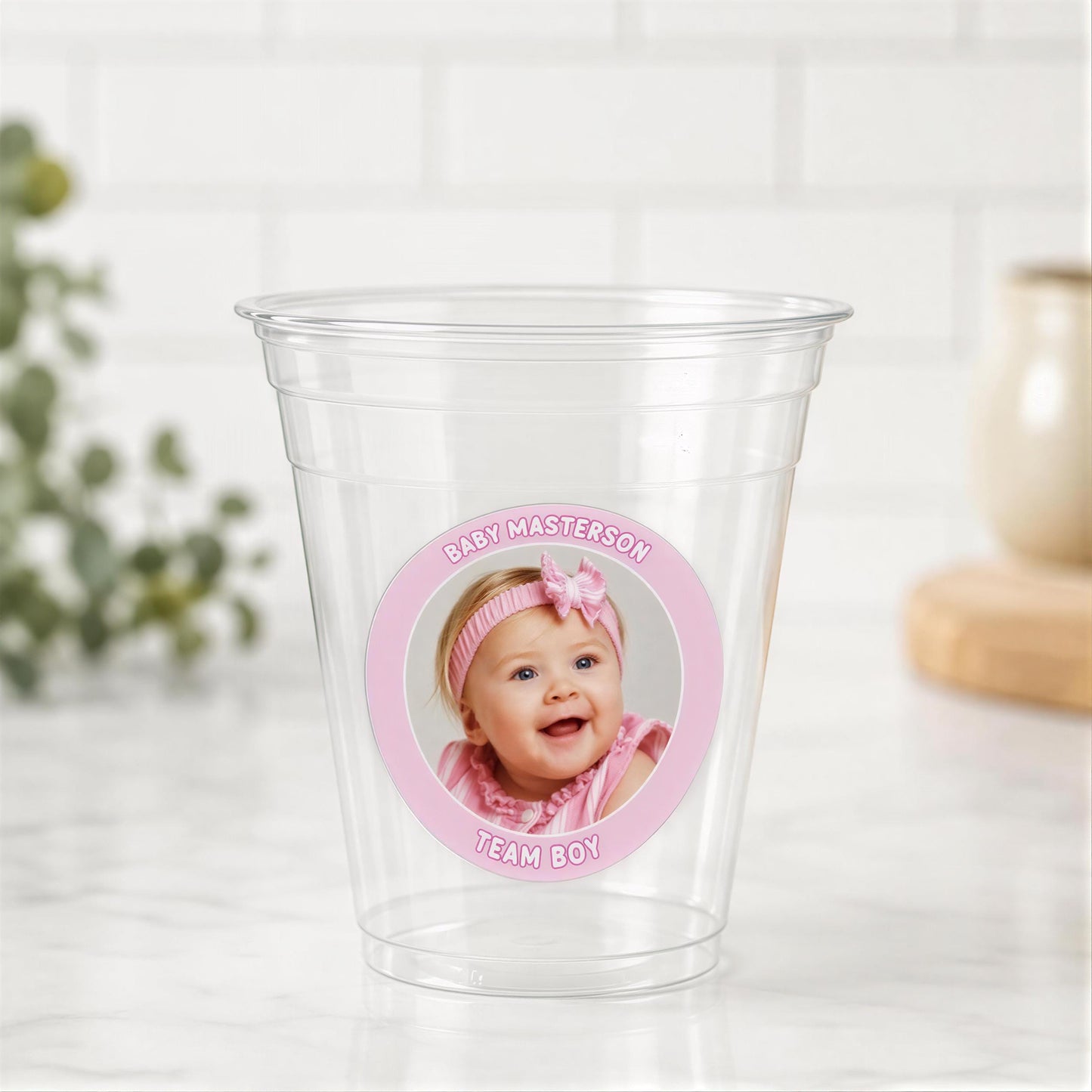 A clear plastic cup with a pink label featuring a smiling baby girl's face.