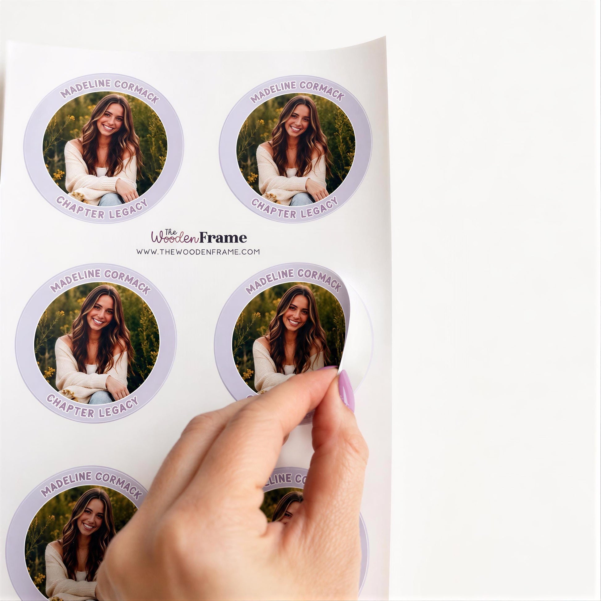 A hand is holding a sticker with a photo of a woman on it, and the sticker is being peeled off a white surface.