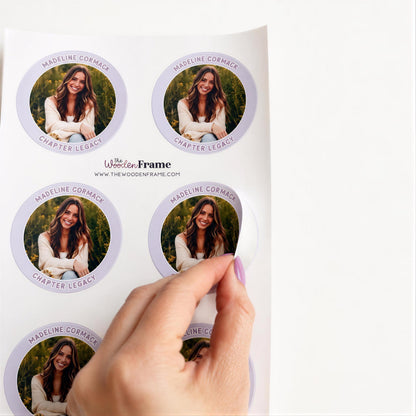 A hand is holding a sticker with a photo of a woman on it, and the sticker is being peeled off a white surface.