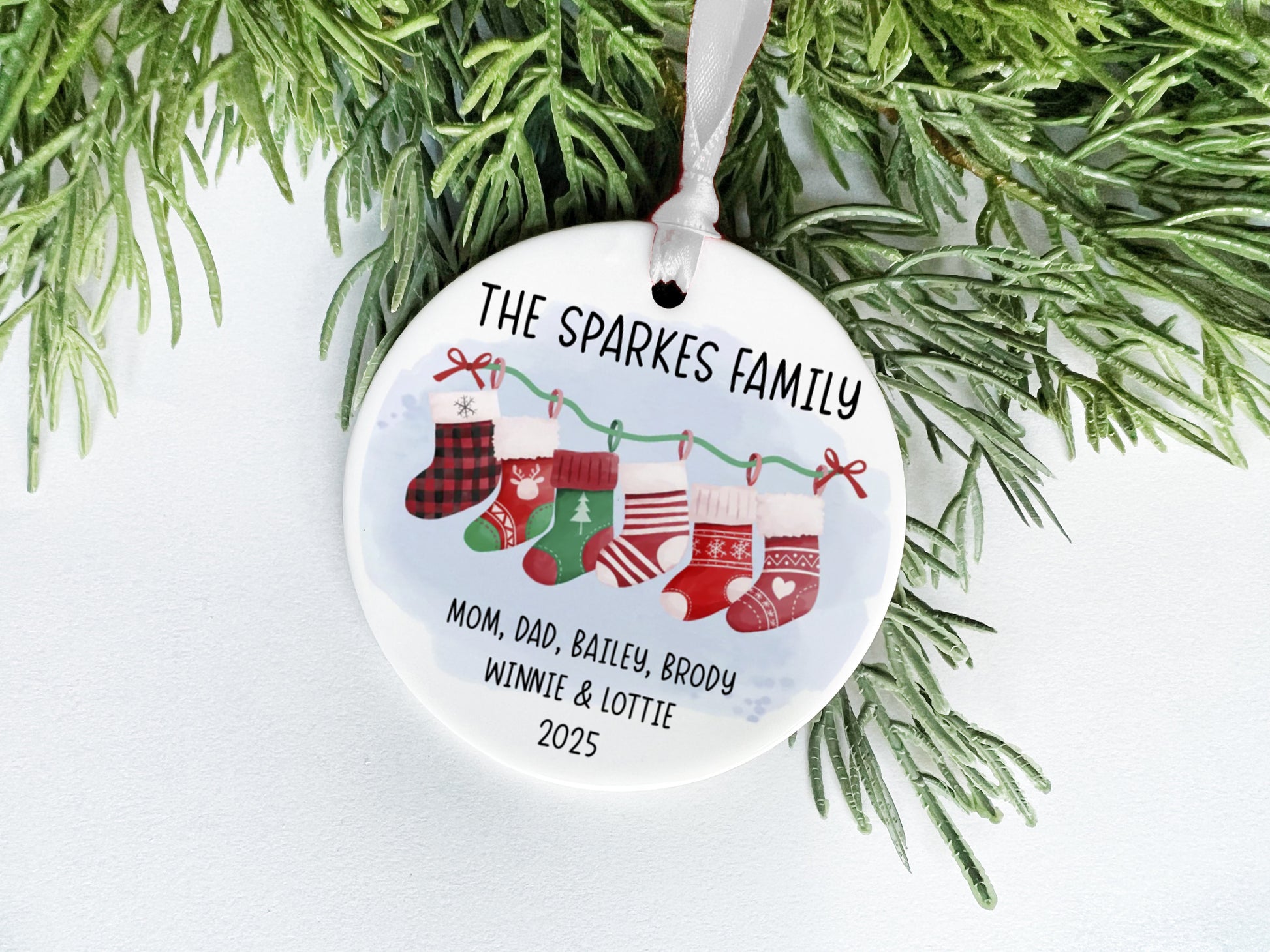 A white ceramic ornament with a Christmas tree branch and greenery, featuring a family tree design with the text "THE SPARKLES FAMILY" and the names "MOM, DAD, BAiley, BRODY, WINNIE & LOTTIE" along with the year "2025".