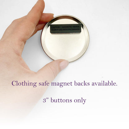 A hand holding a round, silver-colored object with a black label on it, which appears to be a clothing safe magnet back.