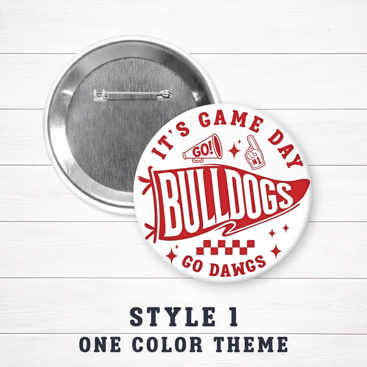 A round pin with a red and white design featuring the text "IT'S GAME DAY BULLDOGS GO DAWGS" and a football fan icon. The pin is set against a white background, and there is a caption below it that reads "STYLE 1 ONE COLOR THEMES".