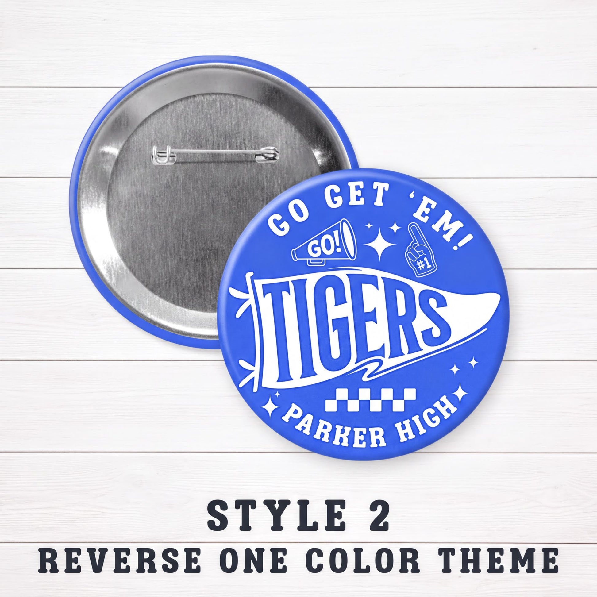 a blue pin with the text "Go Tigers! PARKER HIGH" printed on it, along with a cheerleader design and a checkerboard pattern. The pin is displayed on a white wooden surface, and there is a caption below the image that reads "Style 2 Reverse One Color Theme".