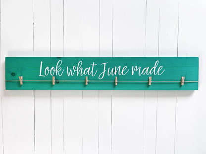 A green wooden sign with the text "Look what June made" written on it, mounted on a white wooden wall.