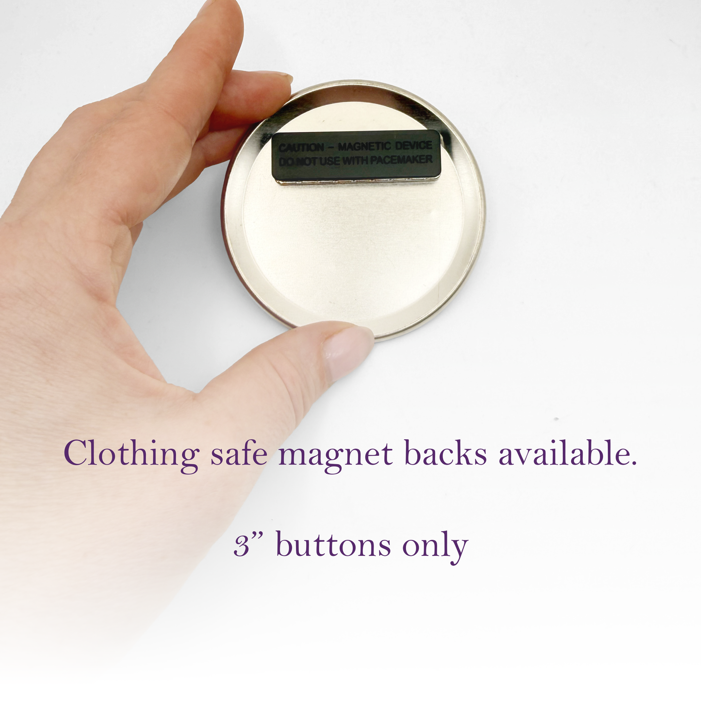 A hand holding a round, silver-colored object with a black label on it, which appears to be a clothing safe magnet back.